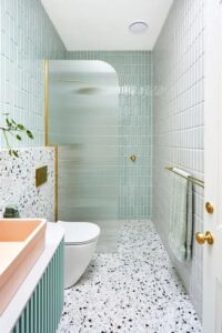 a modern bathroom with mint skinny tiles and white terrazzo, a mint vanity, a blush sink and brass fixtures - Shelterness